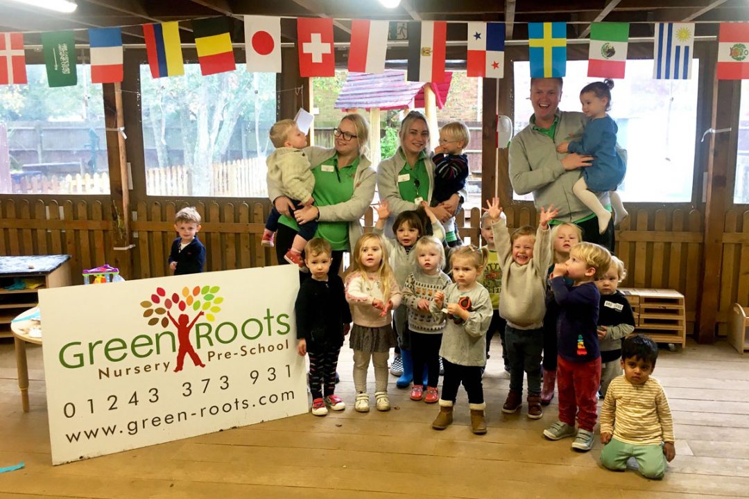 Photo of nursery children and staff standing beside the Green Roots logo